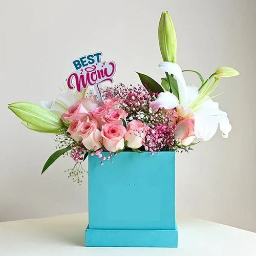 Floral arrangement in a blue box with 'Best Mom' sign on a light background