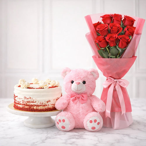 Pink teddy bear, red roses, and cake on a marble surface with a white curtain background