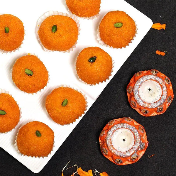 Traditional Indian ladoo sweets with pistachio topping on a white tray, beside decorative candles.