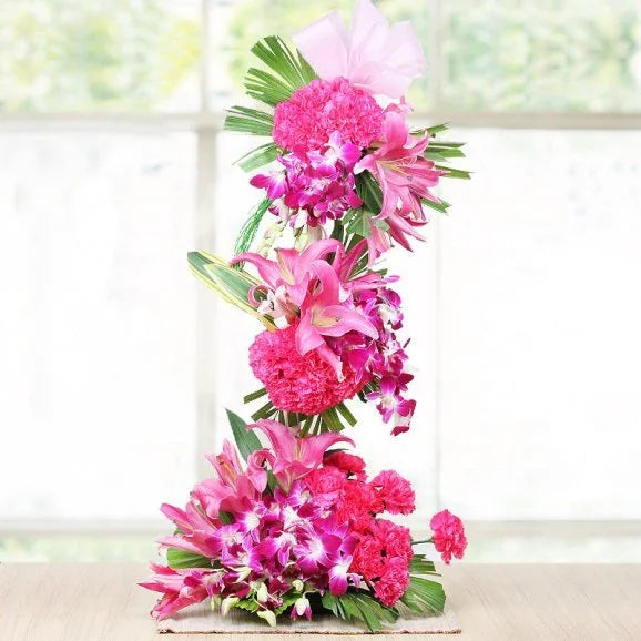 Pink flower arrangement with lilies, carnations, orchids, and green leaves on a table indoors