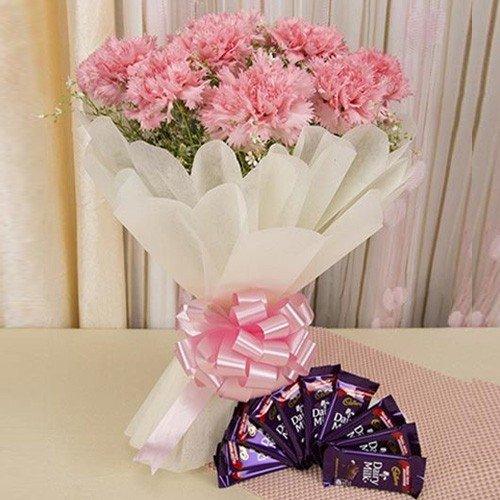 Pink carnation bouquet with pastel wrapping and ribbon, paired with Dairy Milk chocolates, on table