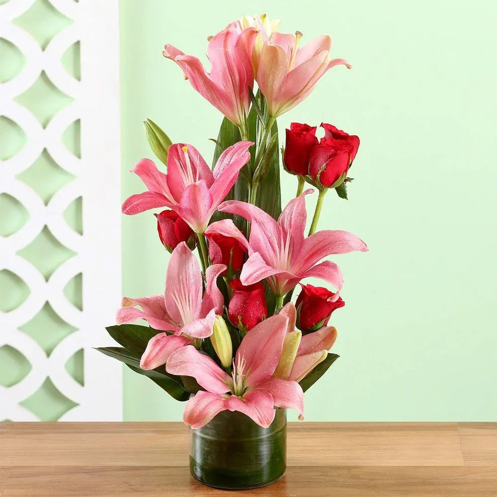 Pink lilies and red roses arranged in a glass vase on a wooden table, flower bouquet gift