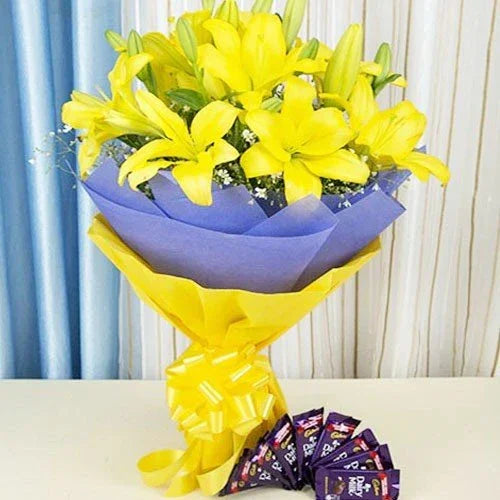 Yellow lily flower bouquet in blue and yellow wrap with assorted chocolate bars gift