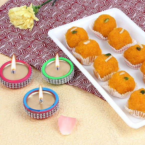 Traditional Indian sweets with decorative candles and yellow flower for festive gifting