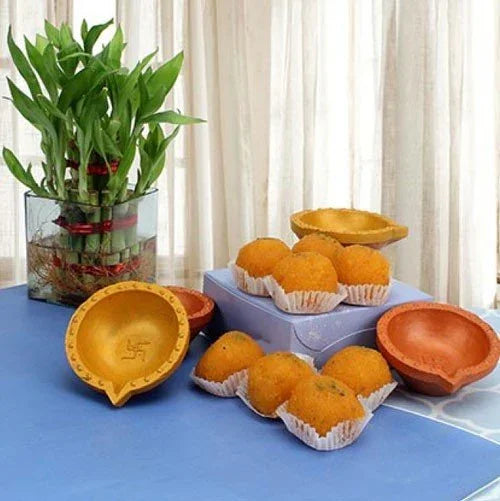 Diwali gift set with lucky bamboo plant, traditional diyas, and Indian sweets on a table