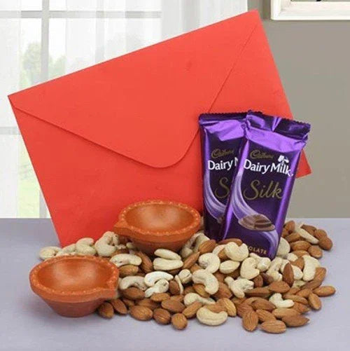 Gift set with red envelope, Cadbury Dairy Milk Silk chocolates, dry fruits, and two clay lamps