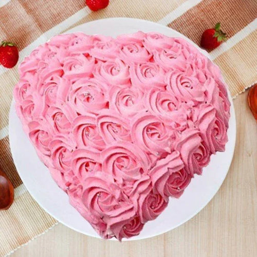 Heart-shaped pink cake with rose patterns on a white plate, surrounded by strawberries on a checkered tablecloth.