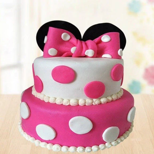 Two-tiered cake with pink polka dots and a large bow, resembling Minnie Mouse, on a light background.