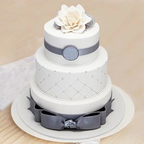 Three-tiered wedding cake with white frosting, gray ribbons, and a large white flower on a beige background.