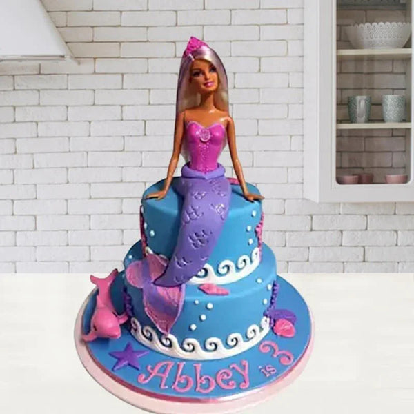 Mermaid-themed birthday cake with a doll on top, featuring blue and pink colors.