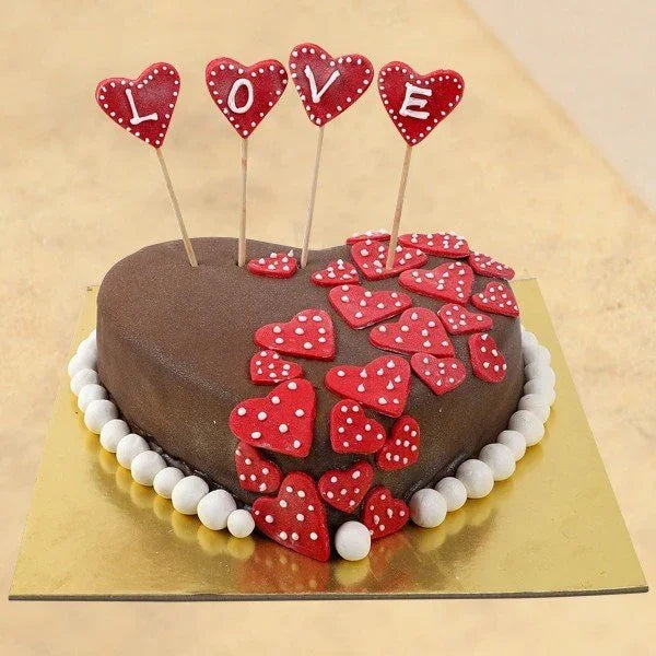 Chocolate cake with red heart decorations and 'LOVE' toppers on a gold tray.