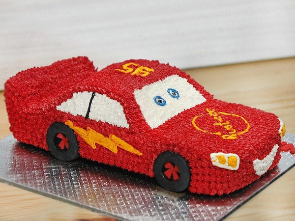 Red car-shaped cake with white and yellow details on a wooden surface