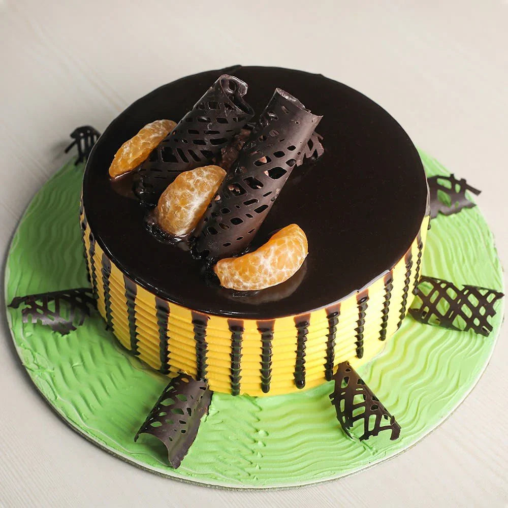 Cake decorated like a bee with black honeycomb, yellow body, and orange accents on a green base.