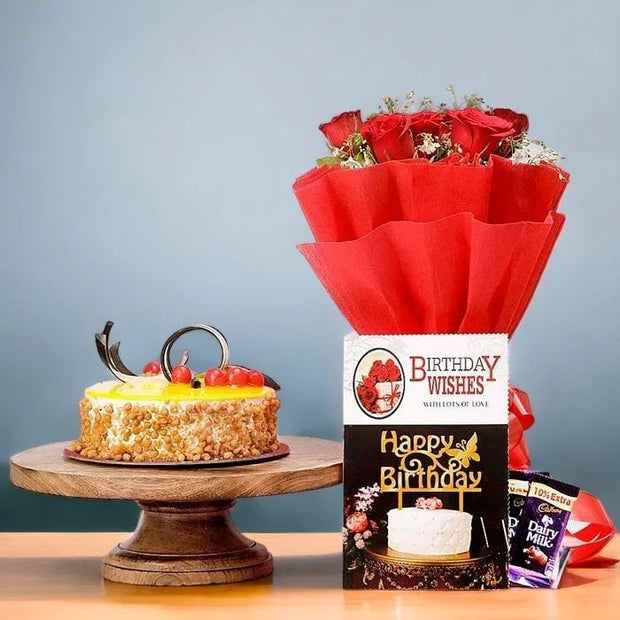 Small birthday cake on a wooden stand with a bouquet of red roses and a 'Happy Birthday' card 