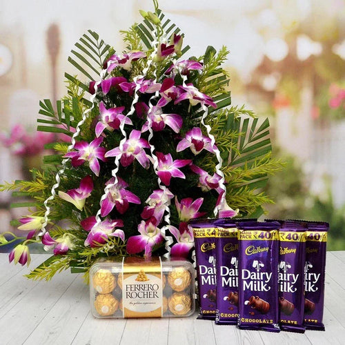Floral arrangement with Cadbury Dairy Milk chocolate bars and Ferrero Rocher on a wooden surface.
