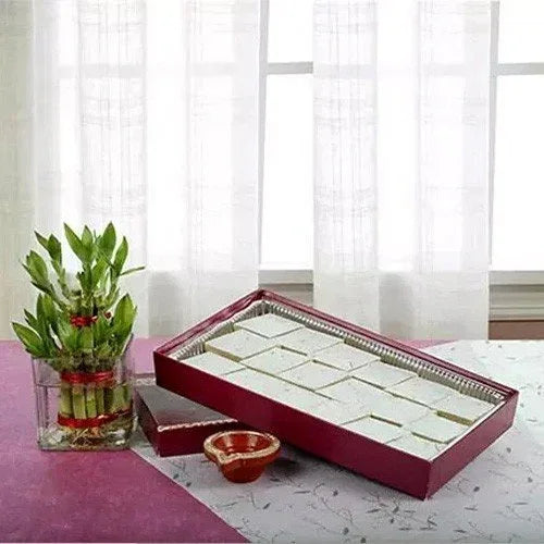 Box of Indian sweets, lucky bamboo plant, and decorative diya on table for gifting