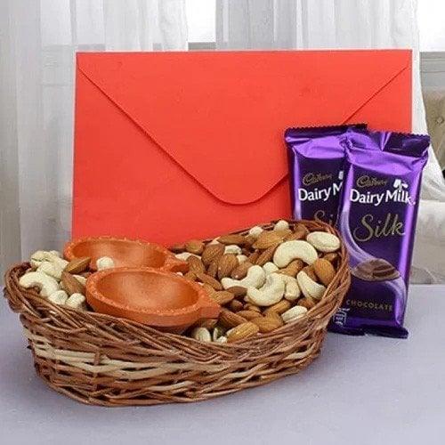 Gift basket with assorted dry fruits, two Dairy Milk Silk chocolates, red envelope, and two clay lamps