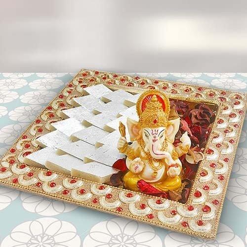 Decorative tray with a Ganesha idol, silver sweets, and rose petals for festive gifting.
