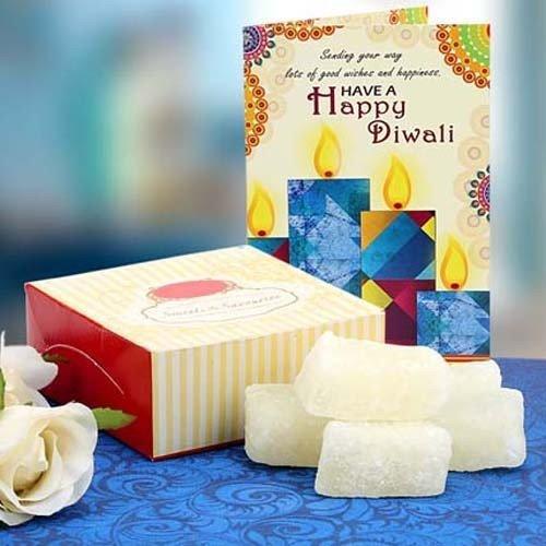 Diwali gift set with sweets, greeting card, and decorative candles on a blue table