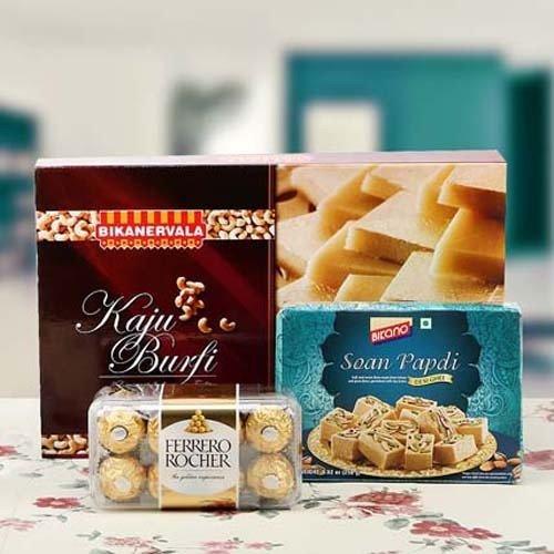 Gift hamper with Kaju Burfi, Soan Papdi, and Ferrero Rocher chocolates on a table