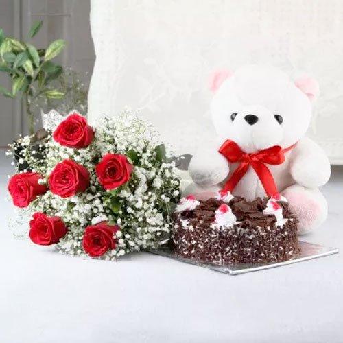 Bouquet of red roses, chocolate cake, and white teddy bear with red bow on table