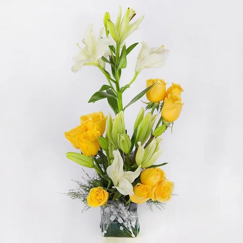 Bouquet of yellow roses and white lilies in a clear vase on a light gray background