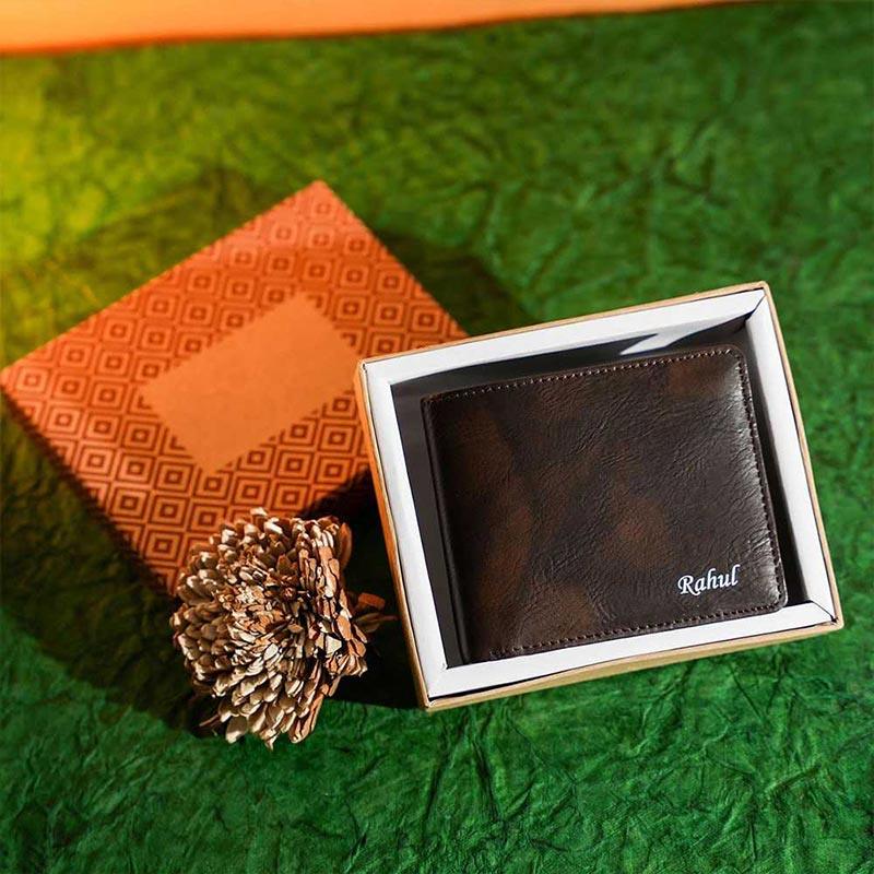 Brown leather wallet with 'Rahul' engraving in a decorative box on a green textured surface.