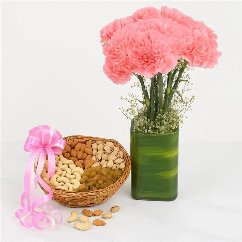 Bouquet of pink flowers in a green vase next to a Dry Fruits basket of assorted nuts on a white background
