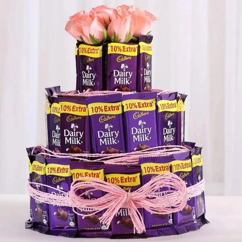 Three-tiered chocolate cake made of Cadbury Dairy Milk bars with pink roses on top against a white background.