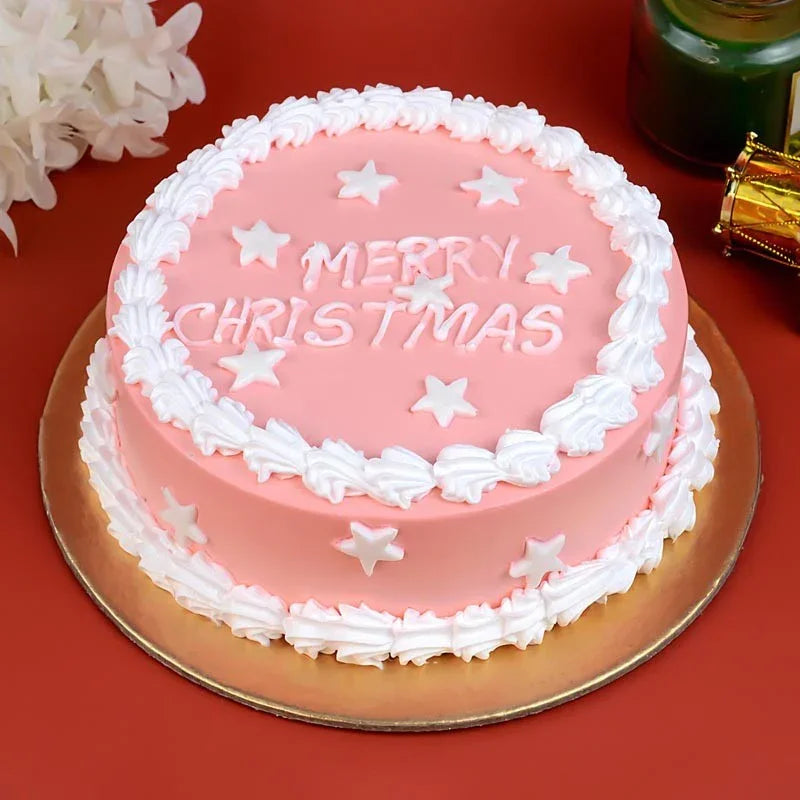 Pink Christmas cake with white frosting and 'Merry Christmas' text on a red surface.