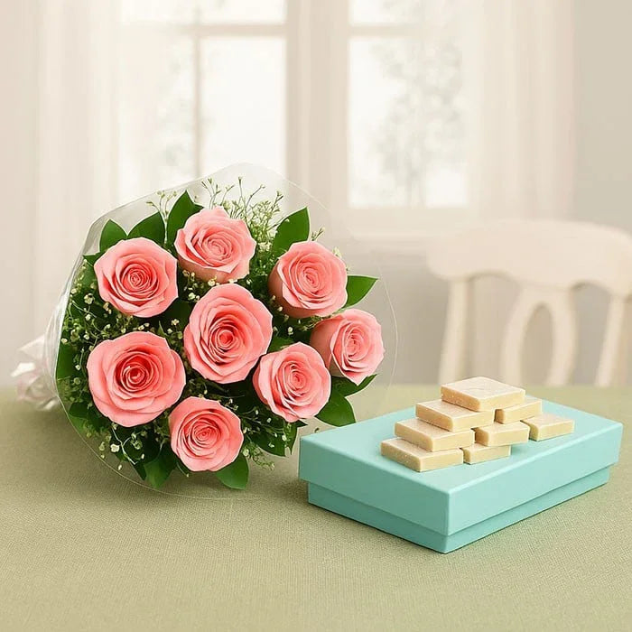 Bouquet of pink roses with box of kaju katli sweets on a table, ideal for gifting.