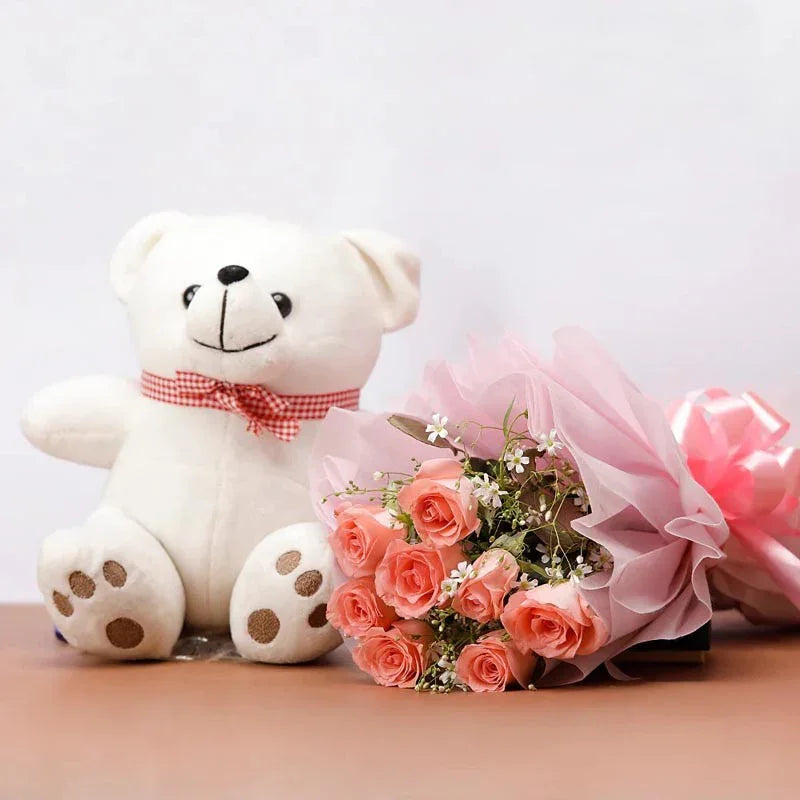 White teddy bear with a pink bow next to a bouquet of pink roses on a light background