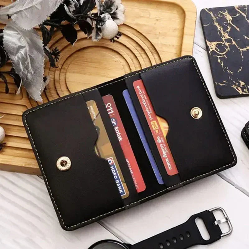 Black wallet with card slots on a wooden surface with flowers and a watch.