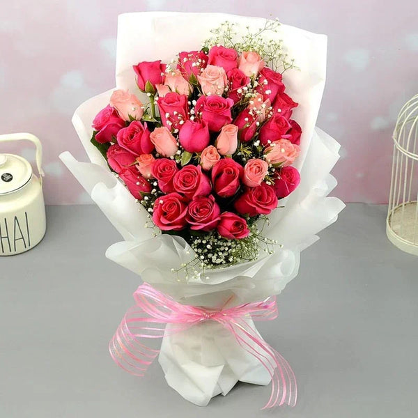 Bouquet of pink and red roses with a white ribbon on a gray surface.