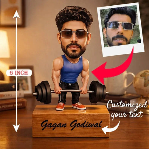 Bobblehead of a man lifting weights with customizable text on a wooden base, set against a blurred indoor background.