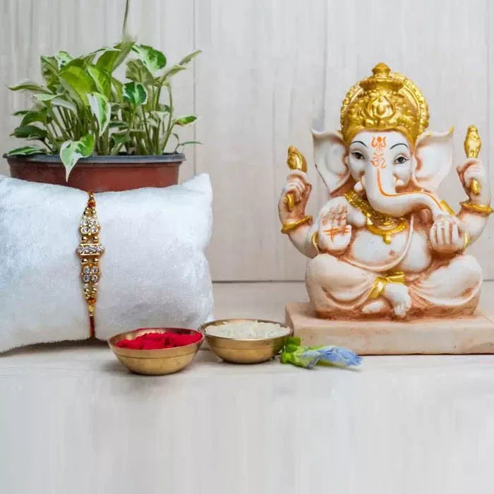 Ganesh statue with offerings on a white surface, next to a plant and decorative items.