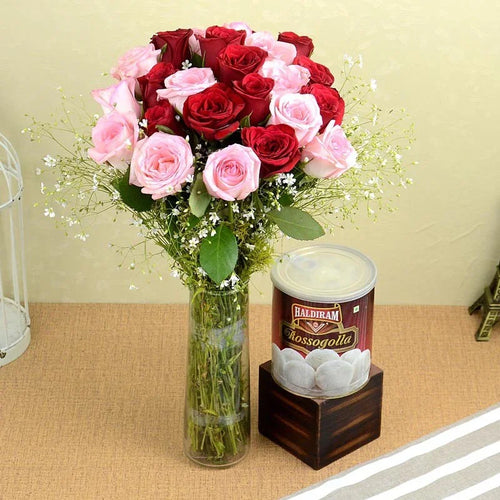 Bouquet of red and pink roses in a vase next to a Haldiram Rosogolla container on a table.