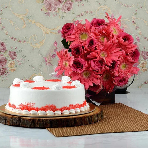 White cake with red decorations next to a bouquet of pink flowers on a floral-patterned wall.