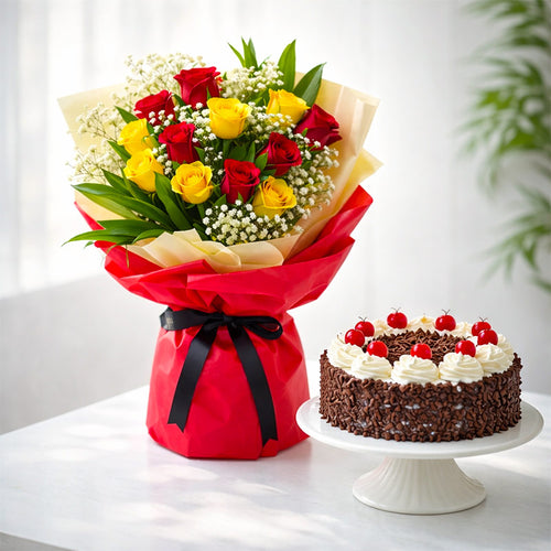 Bouquet of red and yellow roses with a black ribbon, next to a chocolate cake with white frosting and red berries on a white surface.