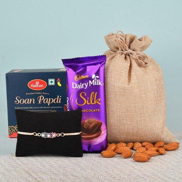 Gift combo with Soan Papdi, Dairy Milk Silk chocolate, almonds, jute pouch, and a rakhi bracelet