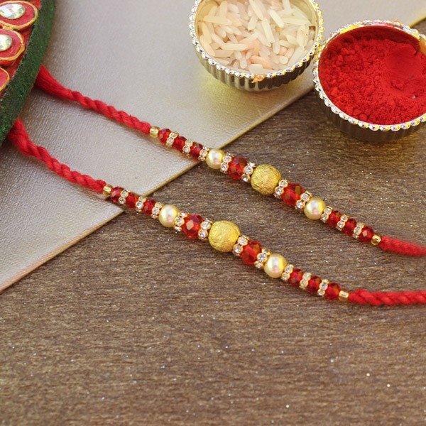 Pair of red and gold beaded rakhi with pearls, rice and kumkum for Raksha Bandhan.