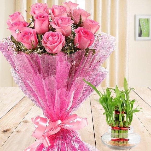 Pink rose bouquet with decorative wrapping and lucky bamboo plant on wooden table