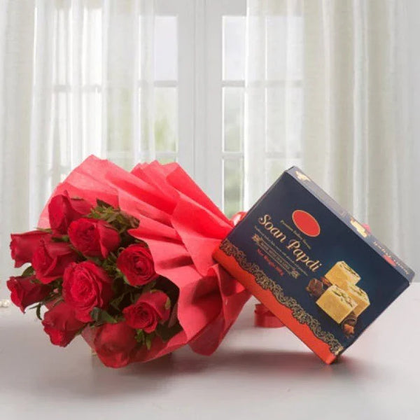 Bouquet of red roses with a box of Soan Papdi sweets on a table by a window