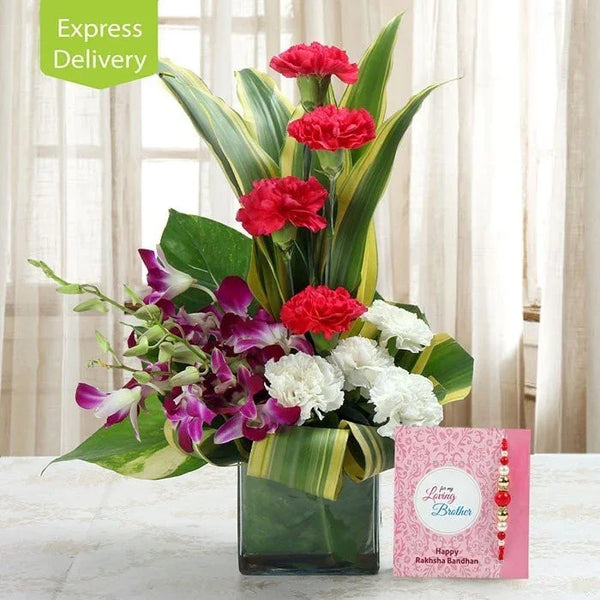 Fresh flower arrangement with red carnations, white flowers, orchids, green leaves in a glass vase, Raksha Bandhan greeting and rakhi