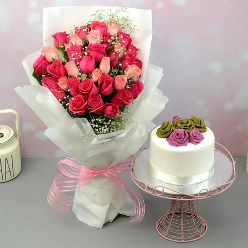Bouquet of pink roses and a small white cake with pink and green roses on a stand against a light pink background.