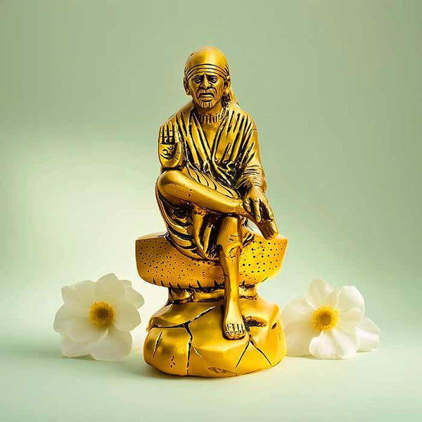 Brass idol of Sai Baba seated on a pedestal with white flowers on a light background