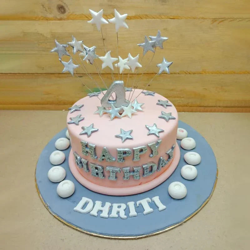 Pink birthday cake with silver stars and 'Happy Birthday Dhriti' text on a wooden background