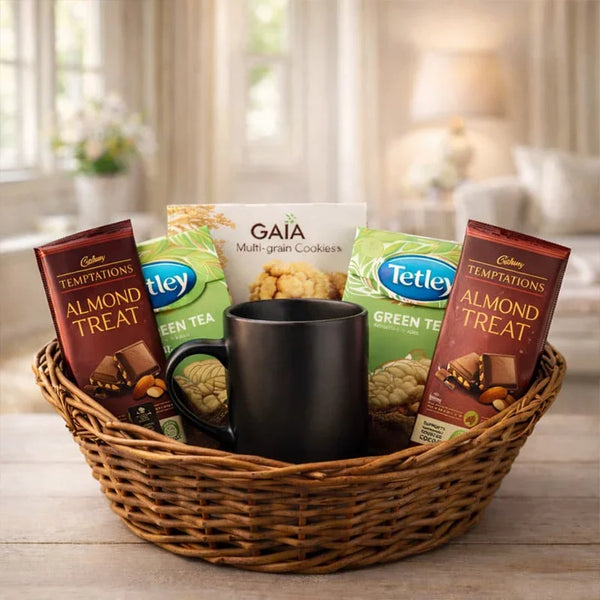 Gift basket with chocolates, green tea, multigrain cookies, and a black mug on a table