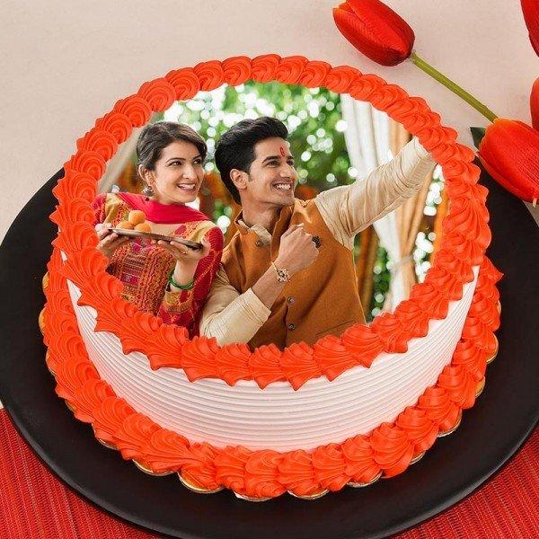 Round photo cake with orange icing, featuring smiling siblings celebrating Indian festival.