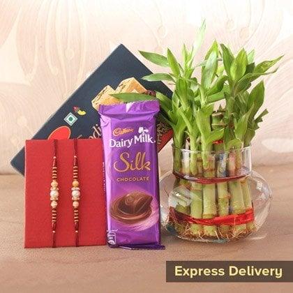 Rakhi set with chocolates, greeting card, and lucky bamboo in glass vase for gift delivery